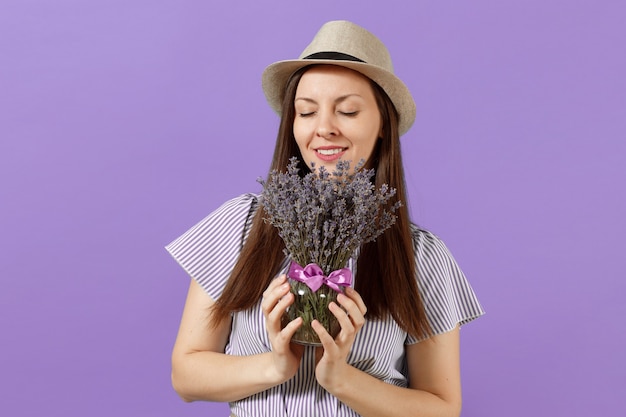 Portrait d'une jeune femme tendre et heureuse en robe bleue, chapeau de paille, tenir et renifler le bouquet de belles fleurs de lavande violettes isolées sur fond violet clair. Concept de vacances de la Journée internationale de la femme