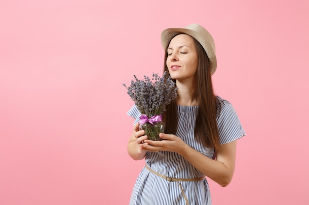 Portrait d'une jeune femme tendre et heureuse en robe bleue, chapeau tenant un bouquet de belles fleurs de lavande violettes isolées sur fond rose tendance vif. Concept de vacances de la Journée internationale de la femme.