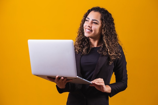 Portrait de jeune femme en tenue de direction avec ordinateur portable sur fond jaune. Femme d'affaires travaillant avec un ordinateur portable