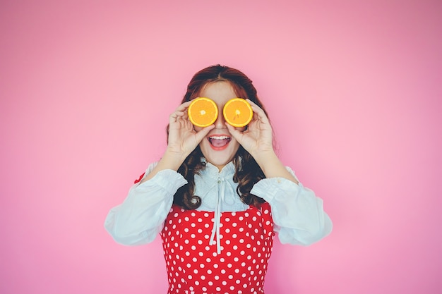 Portrait, de, jeune femme, tenue, oranges, devant, elle, yeux, sur, arrière-plan rose