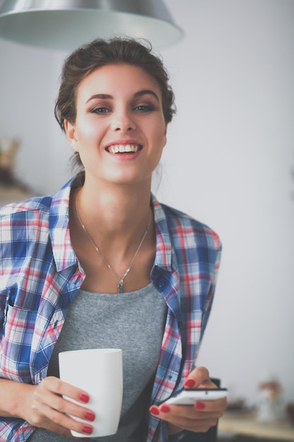 Portrait de jeune femme utilisant un téléphone portable tout en prenant son petit déjeuner dans la cuisine à la maison