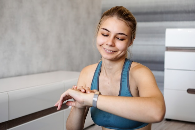 Portrait de jeune femme vérifiant le tracker de fitness numérique pendant l'auto-formation à la maison et souriant