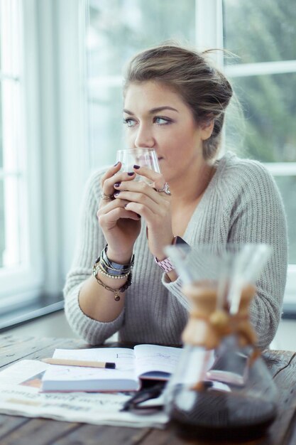 Portrait de jeune femme avec un verre de café regardant par la fenêtre