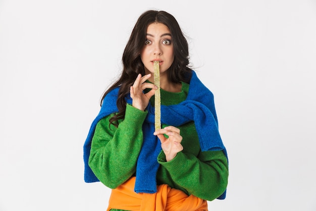 Portrait de jeune femme en vêtements colorés à mâcher de la gomme longue, debout isolé sur blanc