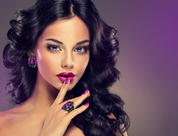 Photo portrait de jeune femme vêtue d'un splendide maquillage de soirée. coiffure dense et ondulée parfaite. maquillage, manucure et bijoux aux teintes violettes.