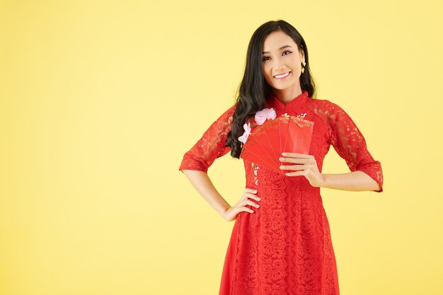 Portrait de jeune femme vietnamienne séduisante avec des enveloppes d'argent chanceuses rouges debout sur fond jaune