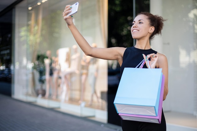 Portrait d'une jeune fille afro-américaine avec des sacs colorés parlant par vidéo au téléphone