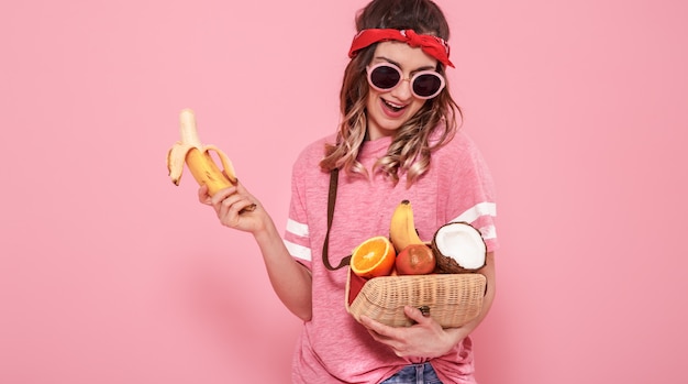 Portrait d'une jeune fille avec des aliments sains, des fruits, sur un mur rose