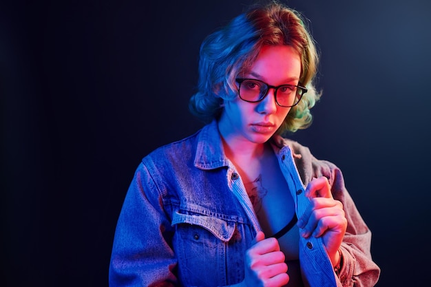 Portrait de jeune fille alternative dans des verres aux cheveux verts en néon rouge et bleu en studio