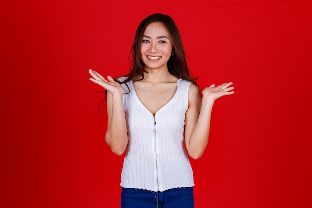 Le portrait d'une jeune fille asiatique charmante et mignonne pose avec un sourire sauvage, montre ses dents et son geste heureux. Studio tourné sur fond rouge.