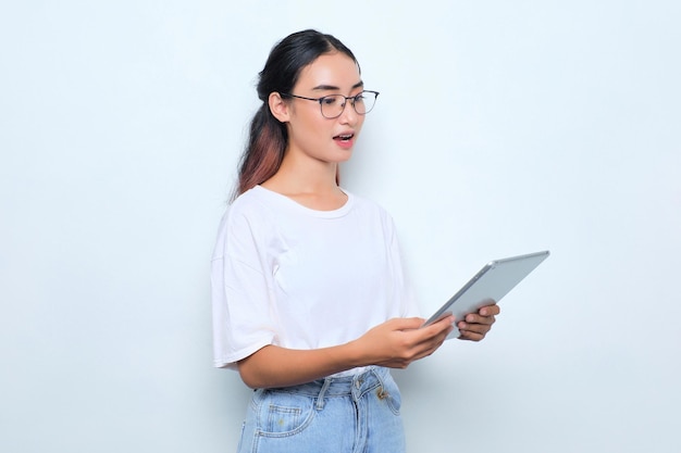 Portrait d'une jeune fille asiatique choquée en t-shirt blanc à l'aide d'une tablette numérique isolée sur fond blanc