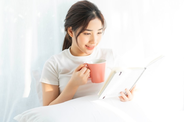 Portrait d'une jeune fille asiatique lisant un livre et buvant du café