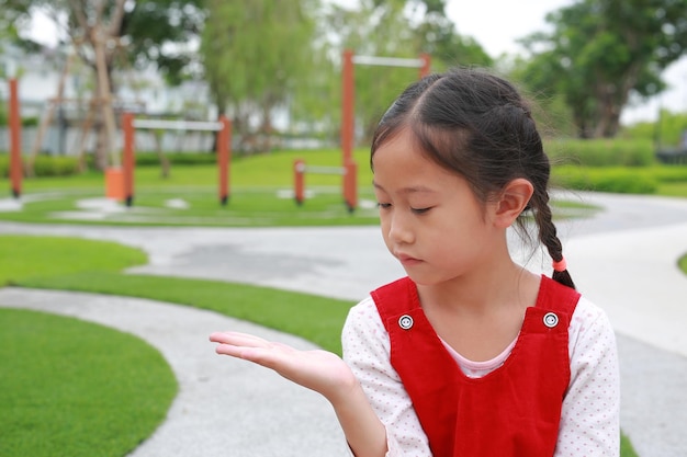 Portrait d'une jeune fille asiatique montrant une main d'expression tenant quelque chose et regardant sans thème dans le jardin