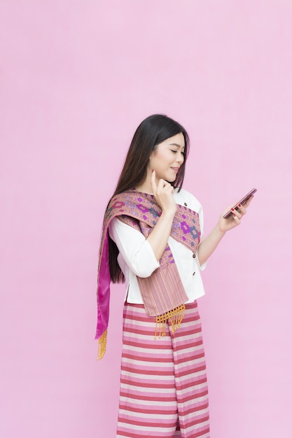 Photo portrait de jeune fille asiatique en robe thaïlandaise traditionnelle et tenant le smartphone sur le dos rose