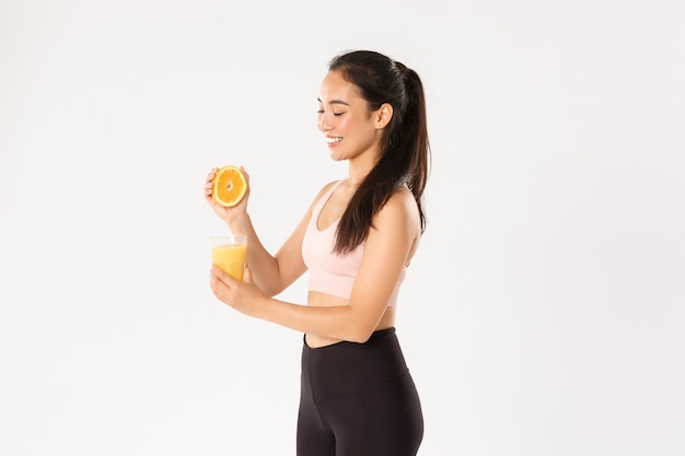 Portrait de jeune fille asiatique saine et mince souriante conseils manger des aliments sains pour le petit déjeuner, gagner de l'énergie pour un bon entraînement, presser le jus d'orange dans le verre.