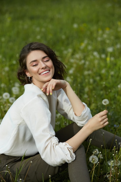 Portrait d'une jeune fille assise dans un champ sur l'herbe de printemps parmi les fleurs de pissenlit.