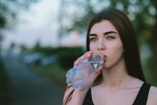 Portrait d'une jeune fille athlétique qui boit de l'eau rafraîchissante par une chaude journée d'été. Mode de vie sportif. Course du matin.