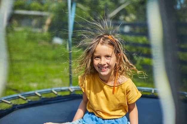 Portrait de jeune fille aux cheveux électrifiés sur trampoline à l'extérieur, dans l'arrière-cour de la maison par une journée d'été ensoleillée, vacances d'été, Joyeux petit enfant sautant sur un trampoline