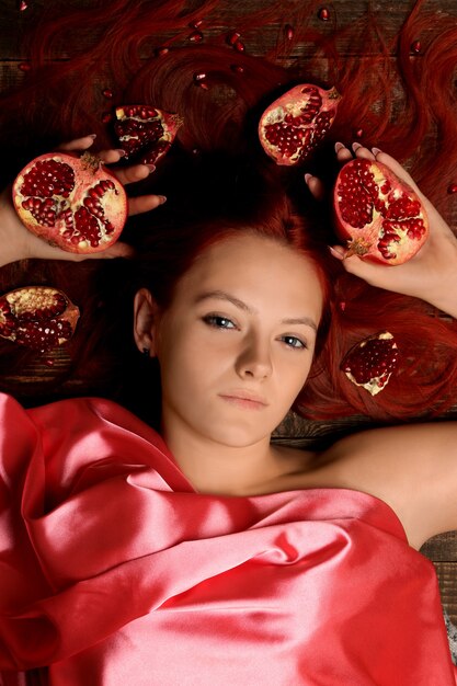 Portrait d'une jeune fille aux cheveux rouges et grenade dans les cheveux sur fond marron