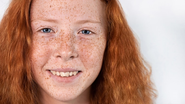 Portrait d'une jeune fille aux cheveux roux avec beaucoup de taches de rousseur sur le visage et les yeux bleus sur blanc