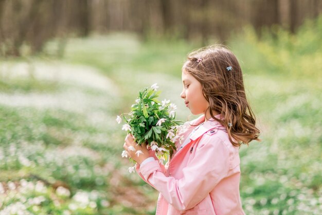 Portrait d'une jeune fille aux primevères. Un enfant dans la forêt printanière renifle un bouquet de fleurs.