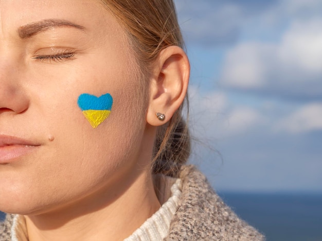 Portrait de jeune fille aux yeux fermés avec drapeau ukrainien jaune-bleu en forme de coeur sur sa joue