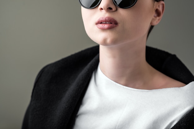 Portrait d&#39;une jeune fille belle dans des lunettes de soleil contre un fond sombre