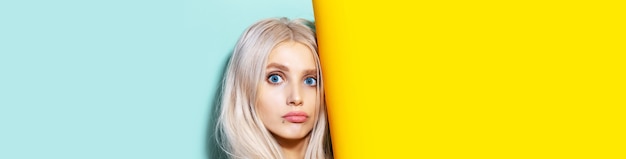 Photo portrait de jeune fille blonde drôle aux yeux bleus. fond de studio panoramique de couleur jaune et aqua menthe.