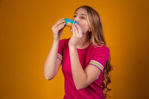 Portrait d'une jeune fille blonde mangeant un délicieux beignets colorés.