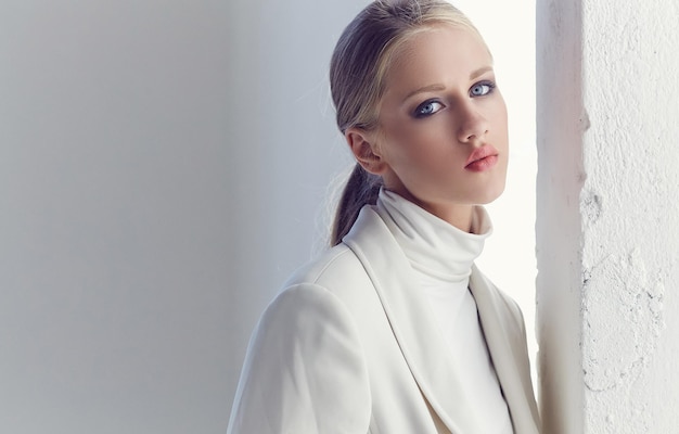 Portrait de jeune fille blonde à la mode aux yeux bleus vêtus de vêtements blancs.