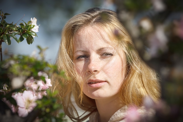 Portrait d'une jeune fille blonde parmi les fleurs d'azalée dans les rayons du soleil