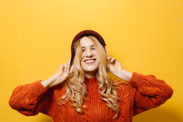 Portrait d'une jeune fille blonde portant une casquette et est vêtu d'un pull rouge et montrant la mode se déplace sur le mur jaune