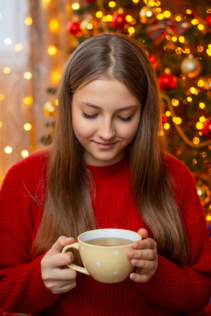 Portrait de jeune fille blonde souriante en pull rouge chaud tenant une tasse de thé dans ses mains