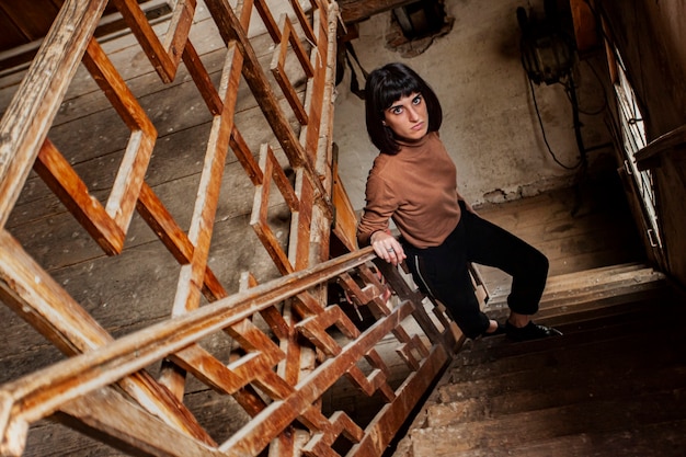 Portrait d'une jeune fille brune dans un escalier d'une maison abandonnée, image en basse lumière