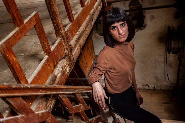 Portrait d'une jeune fille brune dans un escalier d'une maison abandonnée, image en basse lumière