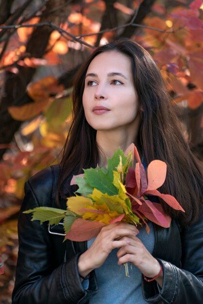 Portrait de jeune fille brune avec des feuilles d'automne dans ses mains. Belle jeune femme en forêt. Cadre vertical.