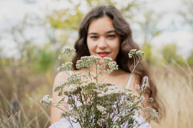 Portrait d'une jeune fille brune sur la nature. Robe blanche et un bouquet de fleurs sauvages dans les mains.