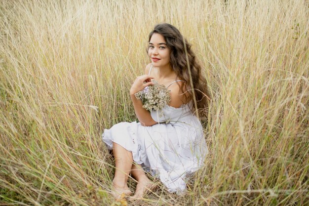 Portrait d'une jeune fille brune sur la nature. Robe blanche et un bouquet de fleurs sauvages dans les mains.