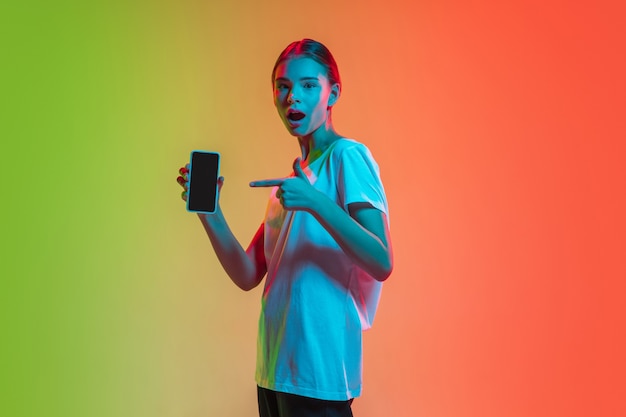 Portrait de jeune fille caucasienne sur fond de studio dégradé vert-orange à la lumière du néon