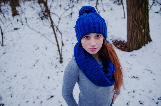 Portrait de jeune fille cheveux roux avec des taches de rousseur porter au bonnet de laine bleu et une écharpe en journée d'hiver.