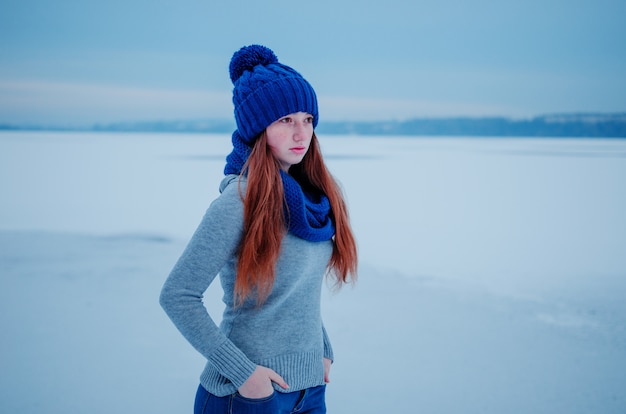 Portrait de jeune fille cheveux roux avec des taches de rousseur porter au bonnet de laine bleu et une écharpe en journée d'hiver.