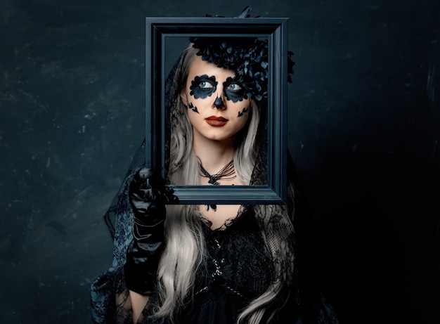 Portrait d'une jeune fille en costume de sorcière avec cadre photo sur fond sombre. Vacances d'Halloween