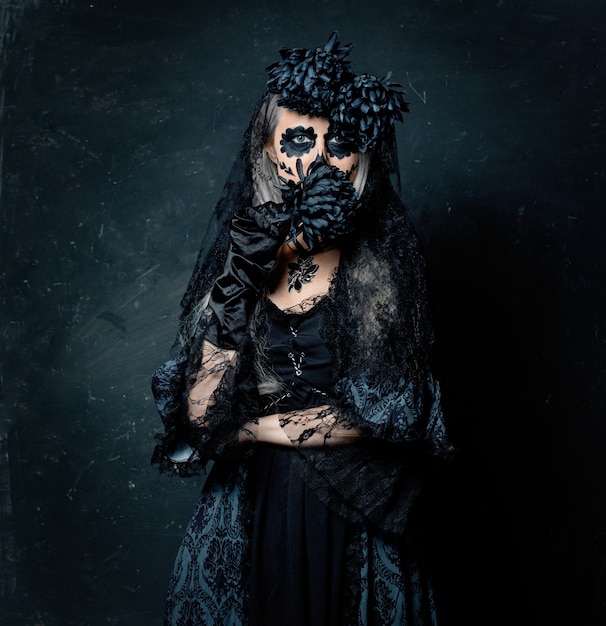 Portrait d'une jeune fille en costume de sorcière avec des fleurs noires sur fond sombre. Vacances d'Halloween