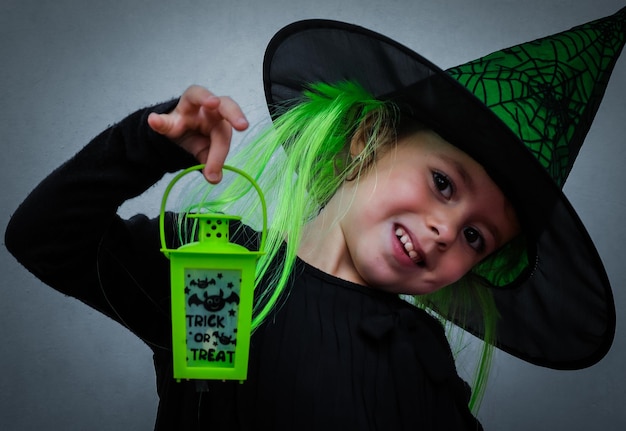 Photo portrait d'une jeune fille dans un chapeau d'halloween tenant une lanterne verte