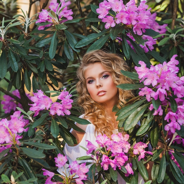 Portrait d'une jeune fille dans un jardin fleuri Un buisson de fleurs est rose rhododendron Beaux cheveux et maquillage