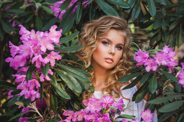 Portrait d'une jeune fille dans un jardin fleuri Un buisson de fleurs est rose rhododendron Beaux cheveux et maquillage