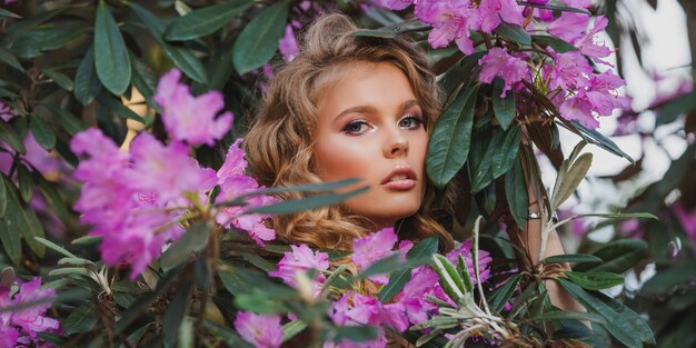 Portrait d'une jeune fille dans un jardin fleuri Un buisson de fleurs est rose rhododendron Beaux cheveux et maquillage