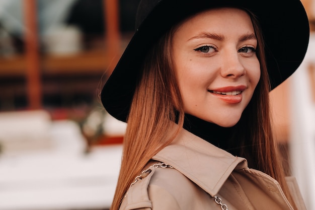 Portrait d'une jeune fille dans un manteau beige et un chapeau noir sur une rue de la ville. Mode de rue pour femmes. Vêtements d'automne Style urbain.