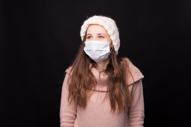 Portrait d'une jeune fille dans un masque médical isolé sur un mur noir.