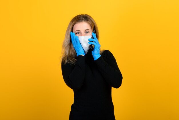 Portrait d'une jeune fille dans un masque médical, qui met un gant en caoutchouc. Fond jaune et gris. Copiez l'espace.